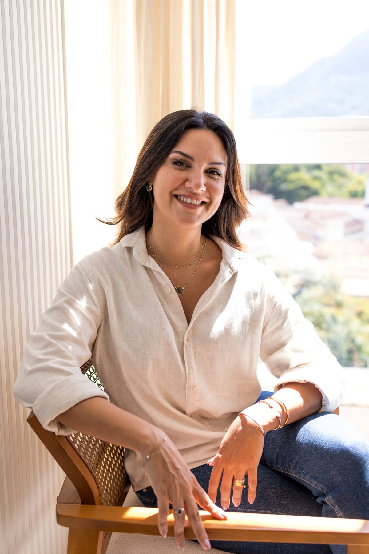 Vivian Dornellas sorrindo, sentada em uma poltrona junto à janela